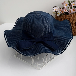 Detail of navy blue straw sun hat featuring wavy brim and elegant silk bow decoration
