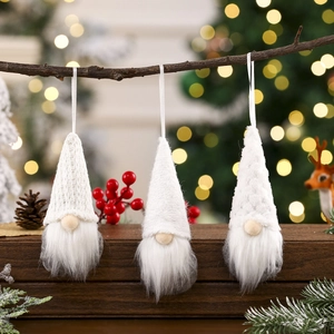 Three white knitted Christmas gnomes with faux fur beards hanging on a rustic branch