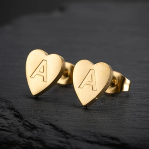 Detailed view of heart-shaped gold stud earring with engraved letter A on slate stone