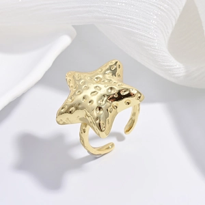 Detailed view of the textured golden starfish open ring on soft white fabric background