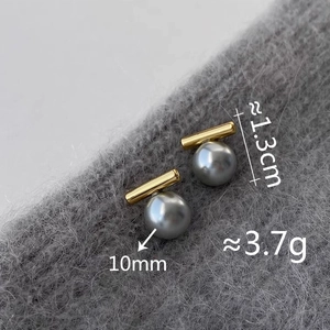 Makro-Detail von Goldbarren- und 10mm grauen Perlenohrringen auf grauem Strick