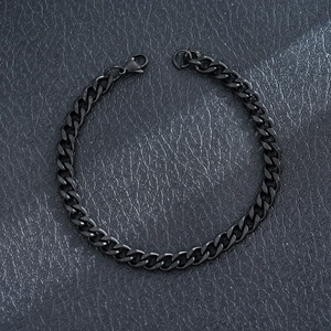 Detailed view of a black stainless steel Cuban link bracelet on a textured surface.