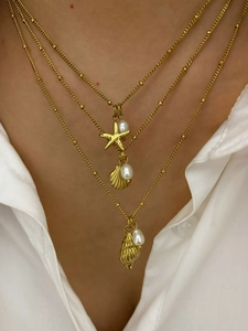 Detailed view of triple-layered gold necklaces with seashell, starfish, and pearl charms