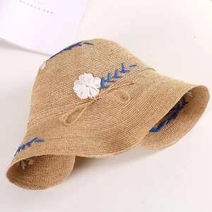 Detail of raffia sun hat with blue geometric stitching and 3D white floral embroidery
