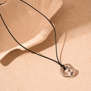 Macro detail of irregular silver pendant with reflective surface on a minimalist background