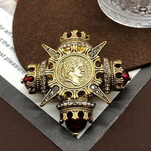 Detail of a gold cross brooch with red gemstone, rhinestones, and Napoleon coin