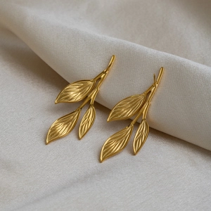 Elegant 18K gold plated leaf stud earrings on beige fabric background