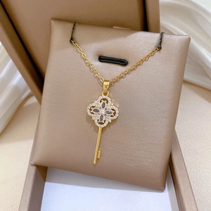 Detailed view of luxury gold clover key pendant necklace with crystals on beige cushion