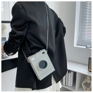 Detail shot of a silver glitter camera-shaped box bag with a metal chain shoulder strap