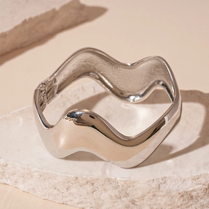 Minimalist silver wave bangle with a hinged closure on a white textured stone surface