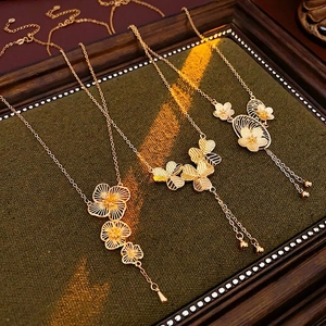 Three gold-plated flower necklaces with elegant tassel pendants on vintage dark wood frame