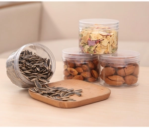 Clear plastic food storage jars with airtight lids containing nuts and seeds on wood