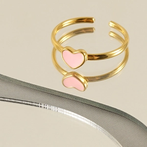 Detailed view of a pink enamel heart ring with a gold adjustable band on a reflective surface