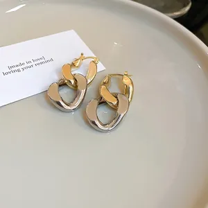 Boucles d'oreilles créoles à maillons dorés et argentés sur un plateau céramique