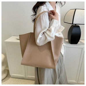 Detail showing beige PU leather tote bag worn by a model in a minimalist room setting