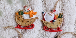 Detail of hand-painted resin snowman and Santa sleigh hanging ornaments on plush background