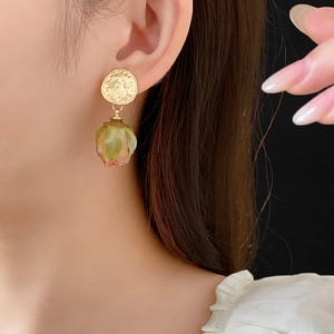 Detail of vintage gold earrings with preserved green rose petals worn by a model