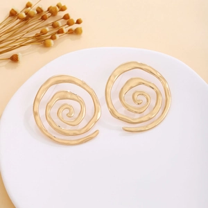 Macro shot of large spiral gold earrings with a metallic finish and hollow floral details