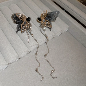 Detail of dark butterfly earrings with silver tassels and rhinestones on velvet