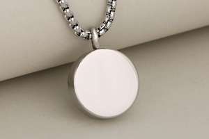 Polished round cremation urn pendant with box chain on neutral beige background