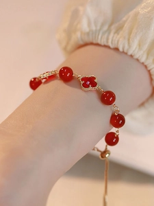 Macro shot of red carnelian clover pendant and gold beaded chain on female wrist