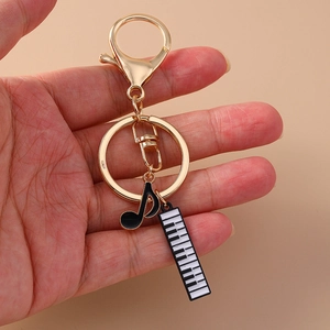 Golden music keychain with black musical note and piano key charms held in hand