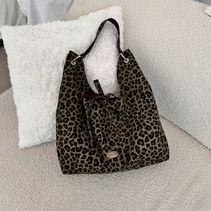 Detail of leopard print tote bag featuring a silver metal logo and wide brown handle