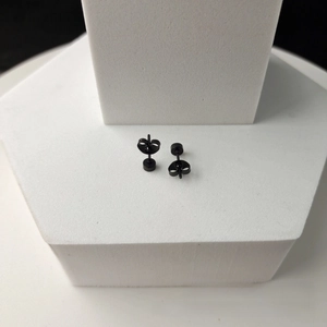 Macro view of minimalist matte black stainless steel disc stud earrings on stone