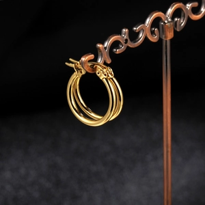 Close-up of golden triple-hoop earrings hanging on a vintage display with black background