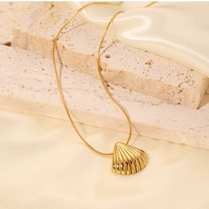 Detail of a golden shell pendant on a thin snake chain over beige silk background