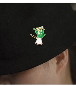 Close-up of lily of the valley enamel pin with a brown coffee pot on a black fabric hat
