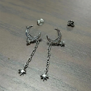Detailed view of silver moon and star tassel earrings with zircons on dark wood surface