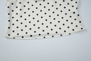 Detailed close-up of white fabric with black polka dots and fine stitching on the garment hem