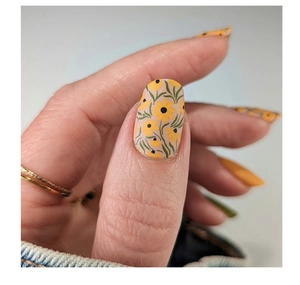 Macro view of matte nude press-on nails with yellow daisies and green leaf patterns