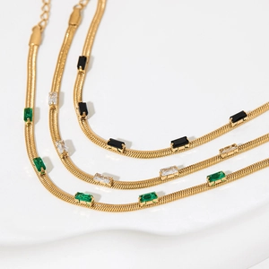 Elegant gold snake chains with green, white, and black rectangular zircon stones on a pedestal