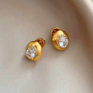 Elegant gold oval stud earrings with white zirconia on champagne silk background
