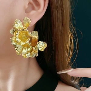 Detailed close-up of oversized gold petal cluster earrings worn by a fashion model