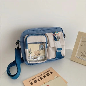 Detail of canvas messenger bag featuring blue and beige patchwork and cute bear brooch