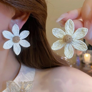 Close-up of white woven flower earrings with beige center worn by a model