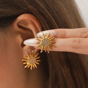 Minimalist gold sun-shaped stud earrings with pavé crystals on a model's ear