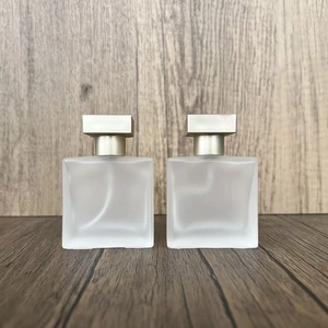 Close-up of two square frosted glass perfume bottles with gold caps on wood surface
