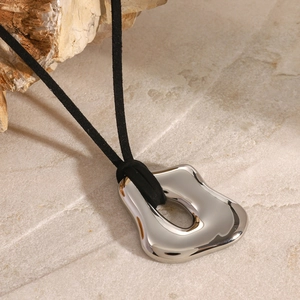Close-up of irregular silver liquid pendant on black cord over natural stone