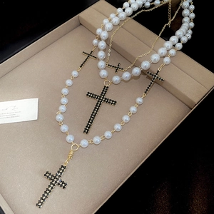 Detailaufnahme einer mehrlagigen Perlenkette mit schwarzen Strass-Kreuzanhängern