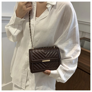 Detail of dark brown V-quilted crossbody bag with metal chain strap on model