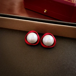 Detailed macro view of white pearls nested in red metal elegant earrings on brown surface