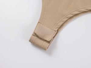 Close-up of snap fasteners and fine stitching on the beige cotton bodysuit's crotch