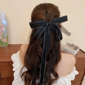 Rear view of a large black mesh bow hair clip with white piping on model hair