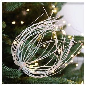 Close-up of sparkling white sequin Christmas tree branch decoration with warm bokeh lights