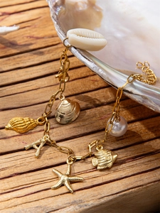 Detail of golden ocean-themed bracelet with shell, starfish and pearl charms