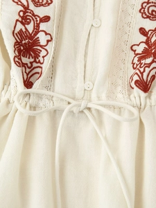 Detail of red floral embroidery and delicate lace stitching on beige cotton blouse